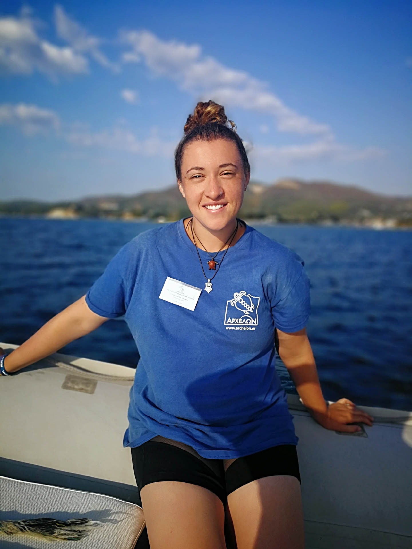 A young woman in a blue polo shirt on a boat in a tropical sea smiles at the camera