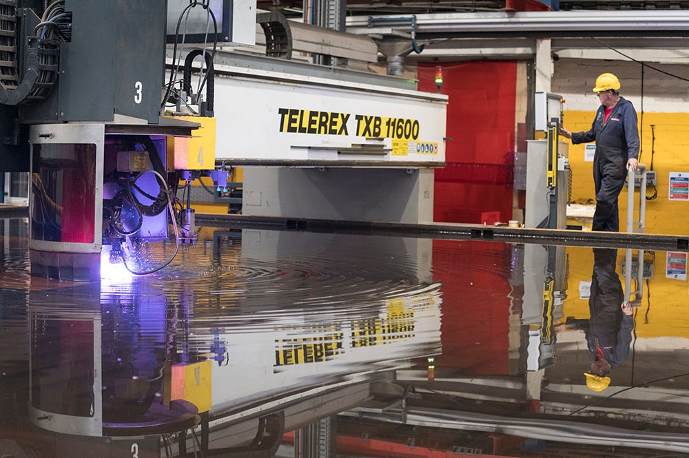 A purple laser cuts through solid steel in a large warehouse