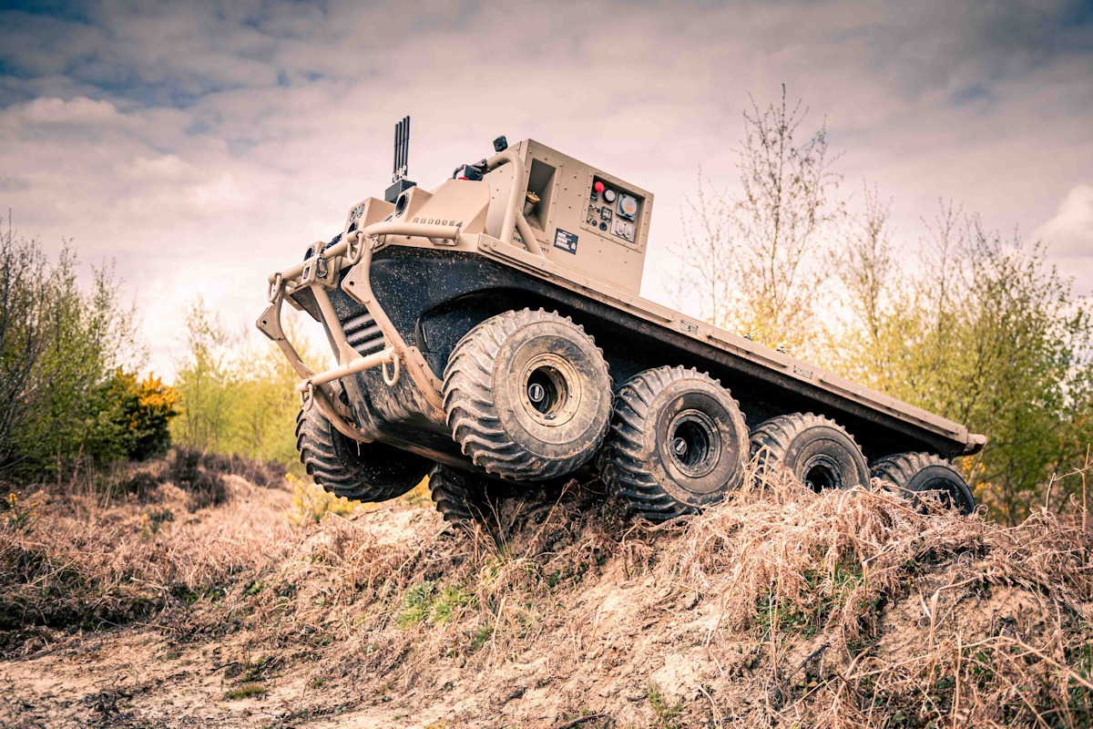 Eight-wheel autonomous vehicle coming over grassy mound during trials