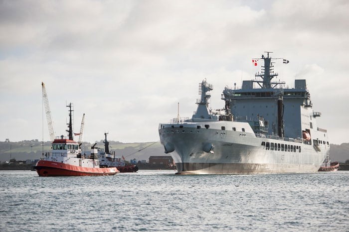 A large grey navy tanker ship being pulled by a tug boat