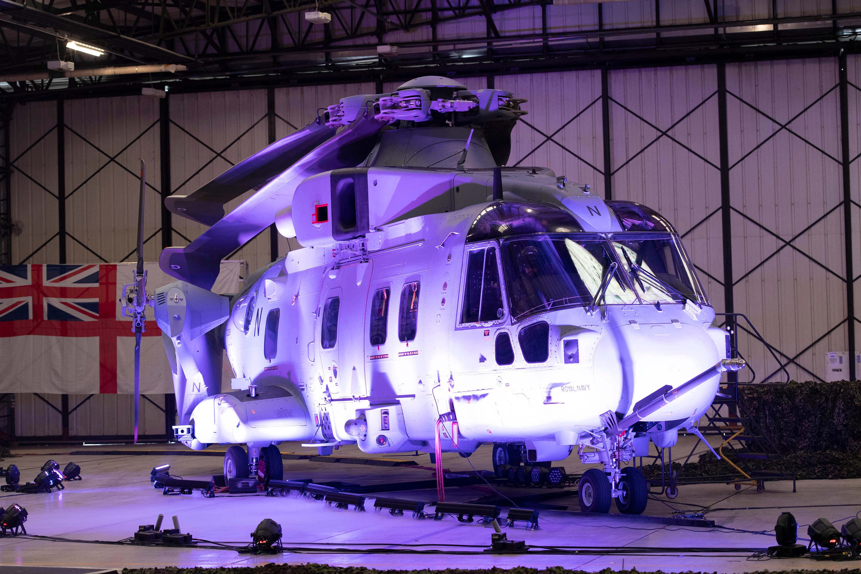 A helicopter lit up by a purple light in a hangar