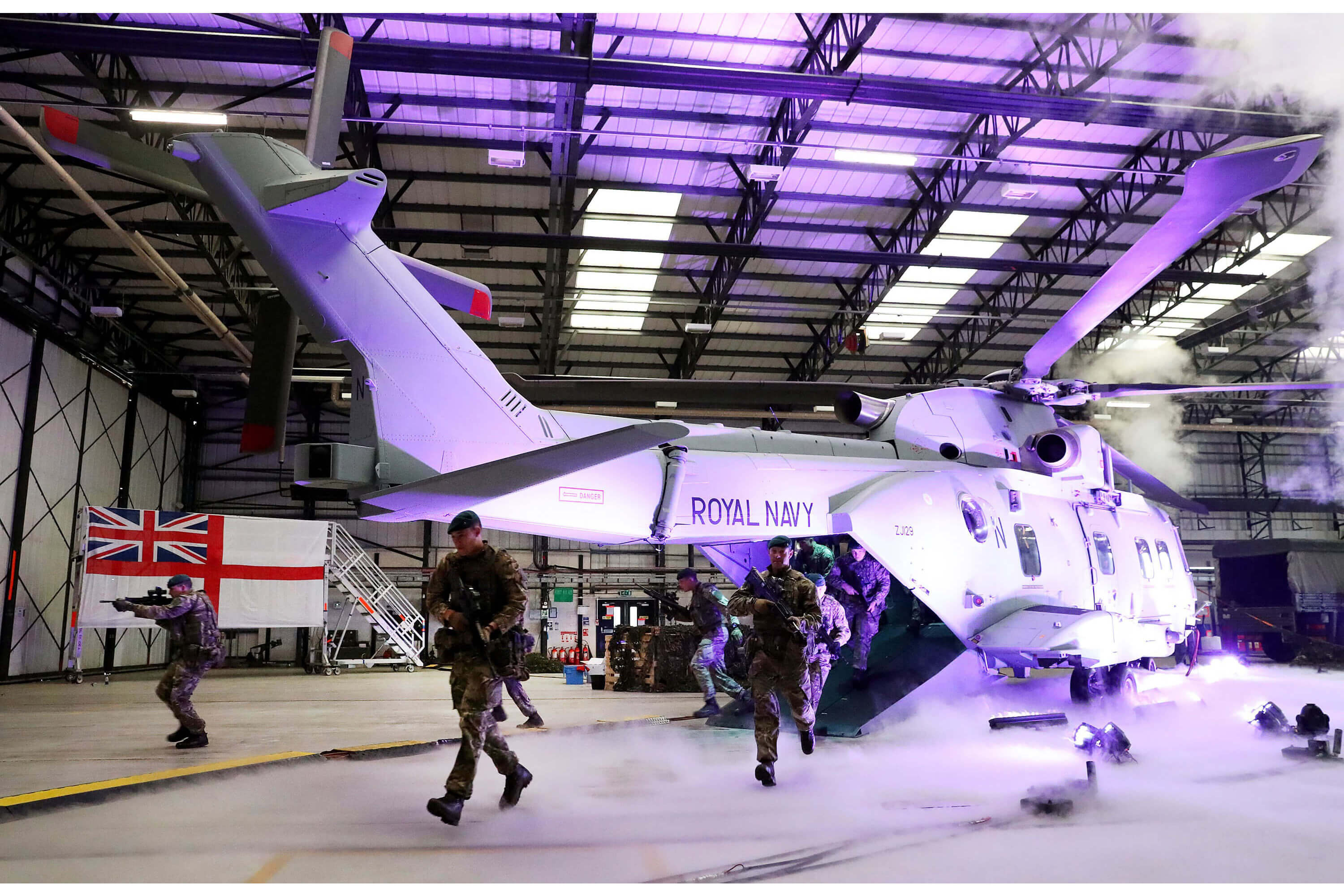 A helicopter lit up by a purple light in a hangar