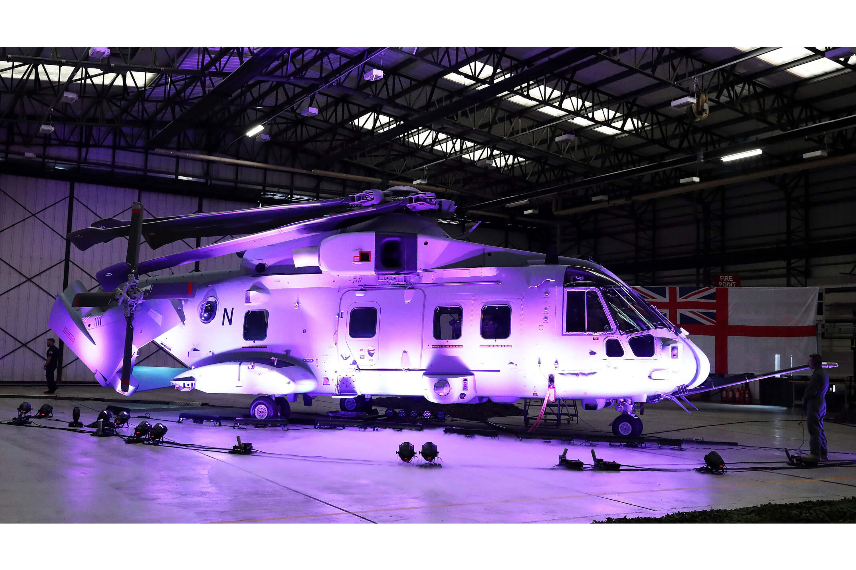 A helicopter lit up by a purple light in a hangar