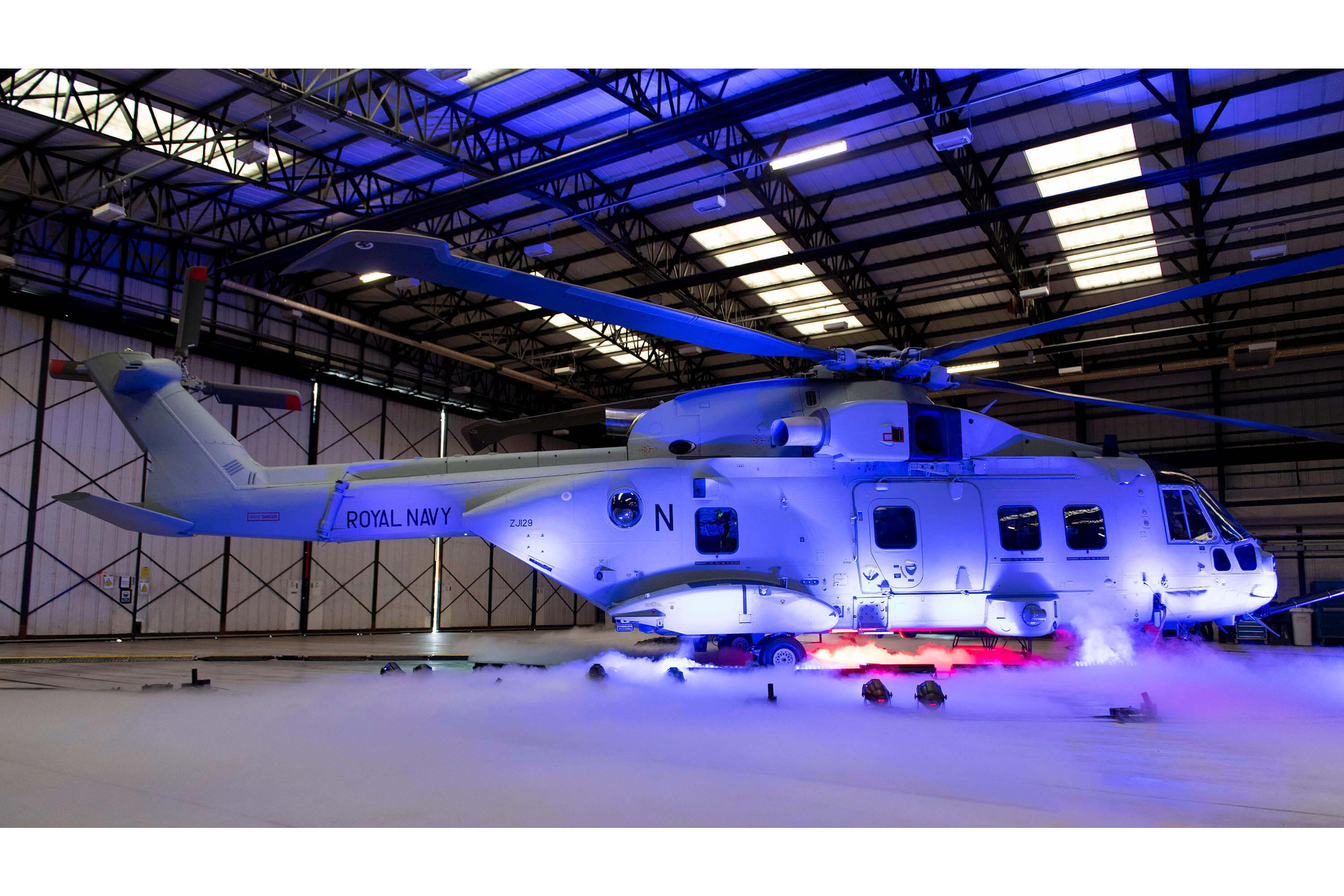 A helicopter lit up by a purple light in a hangar