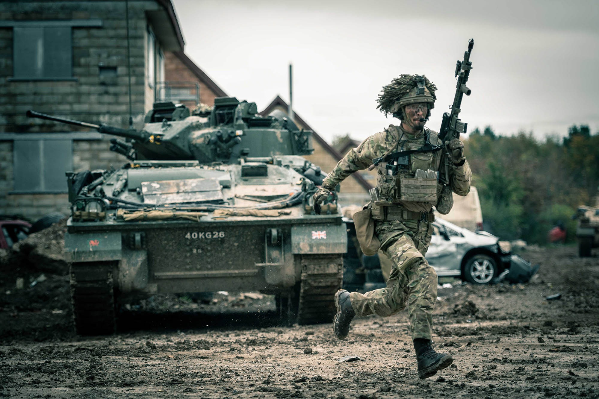 A male soldier running during an outdoor training exercise, holding a gun aloft