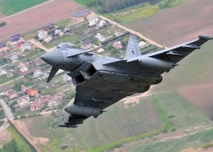 A grey fighter jet plane climbs into the sky with fields disappearing below