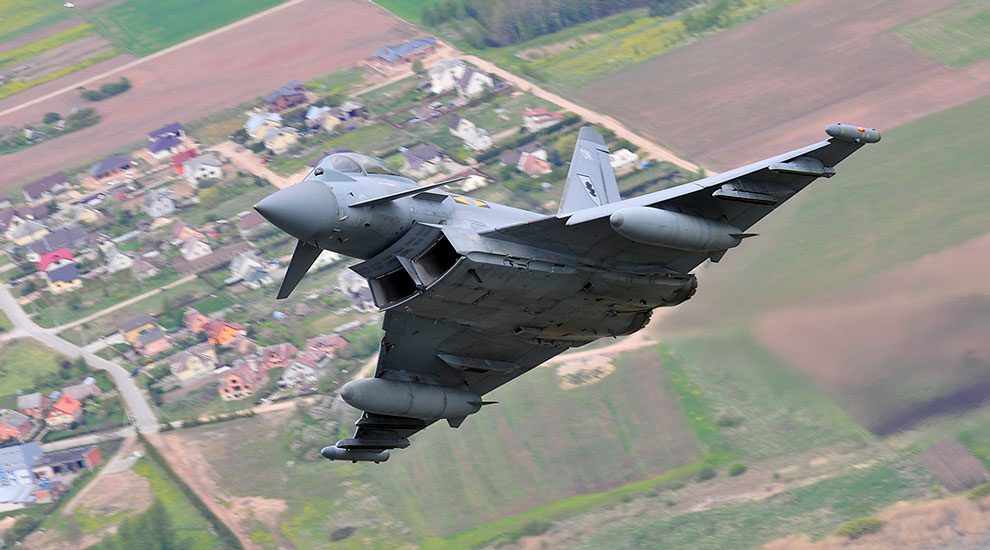 grey military jet flying over countryside