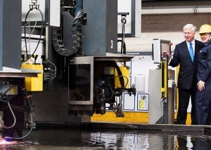 two men in suits press a button to start a laser cutter to cut steel