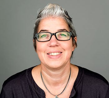 A woman with grey hair and glasses smiling at the camera in a black top