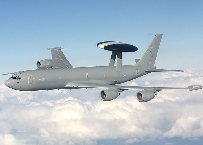 A grey military plane with a radar on top mid flight