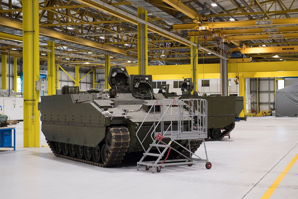 A large green armoured tank stands in a large warehouse with yellow beams
