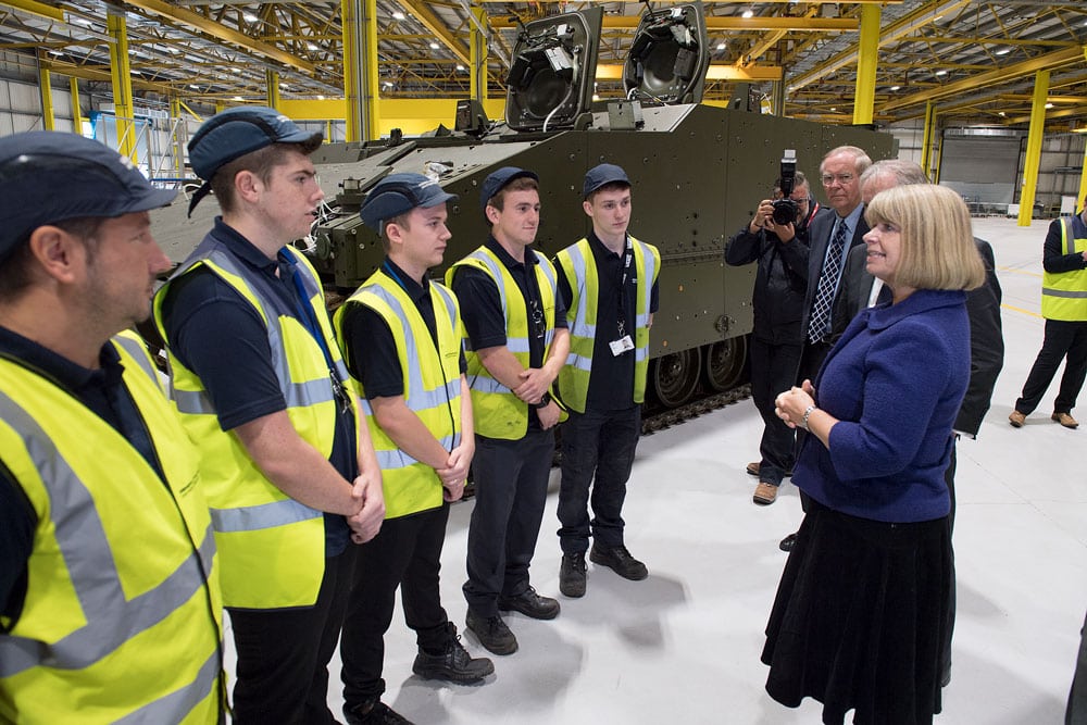 A group of engineers in high visibility jackets are interviewed by a female government minister