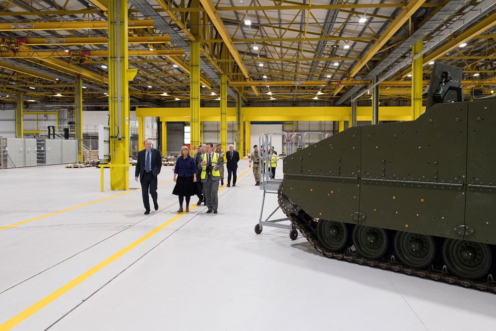 A large green armoured tank stands in a large warehouse with yellow beams