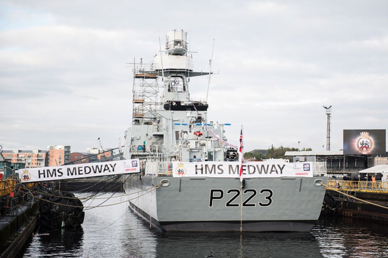 A grey navy ship carrying a banner with "HMS Medway" written on it
