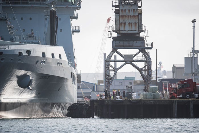 A large grey navy tanker ship next to a crane