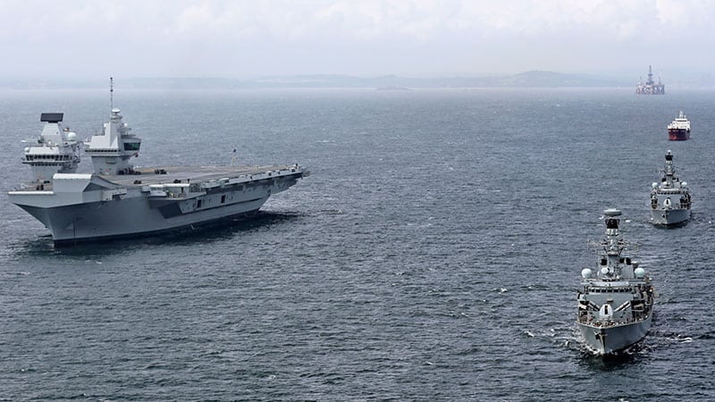 A large aircraft carrier sailing alongside a line of navy boats