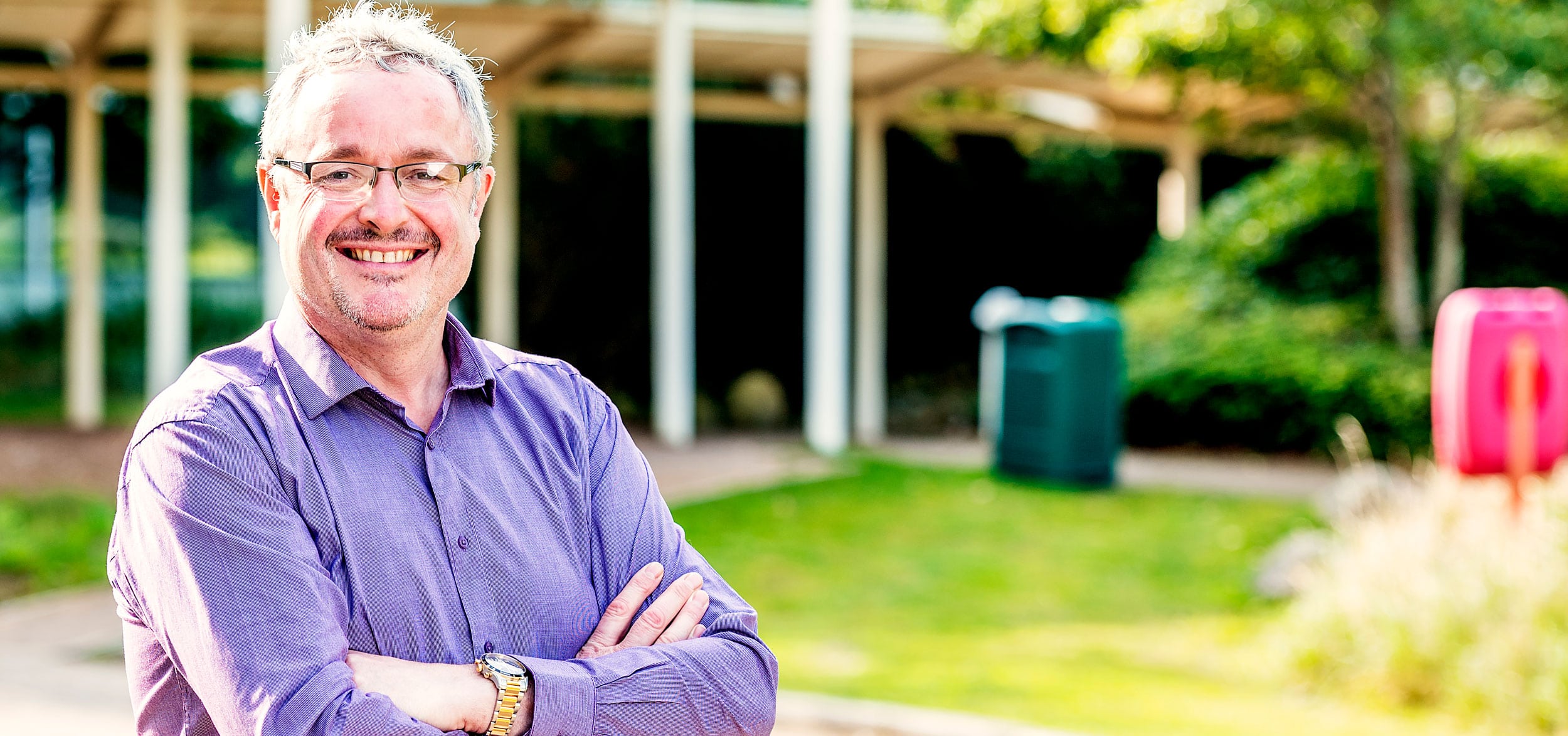 A man in a purple shirt and glasses smiles at the camera