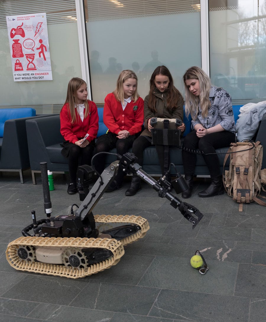 Children drive a bomb disposal robot alongside a military officer