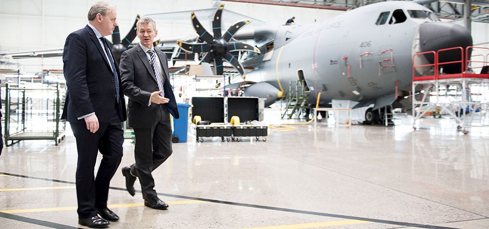 Large military plane in hangar, with men walking in front