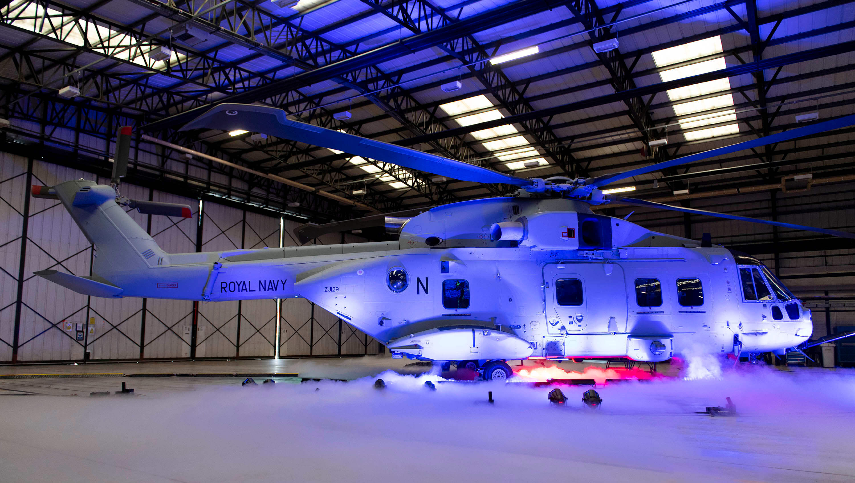 A helicopter lit up by a purple light in a hangar