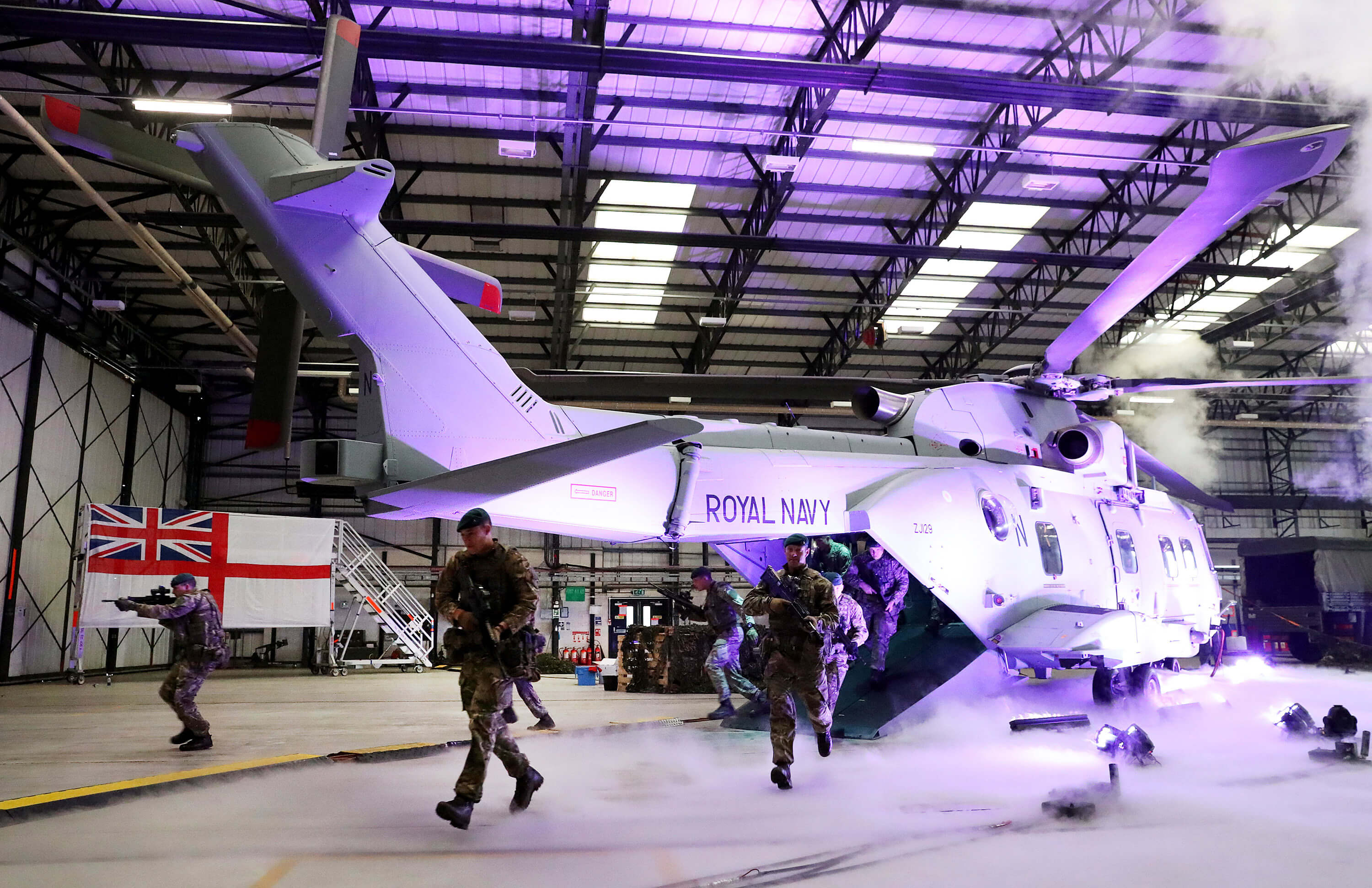 A helicopter lit up by a purple light in a hangar