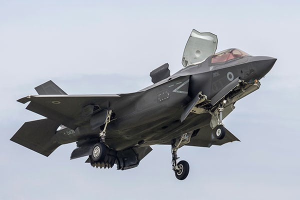 A large grey fighter jet comes into land, wheels and air brakes extended