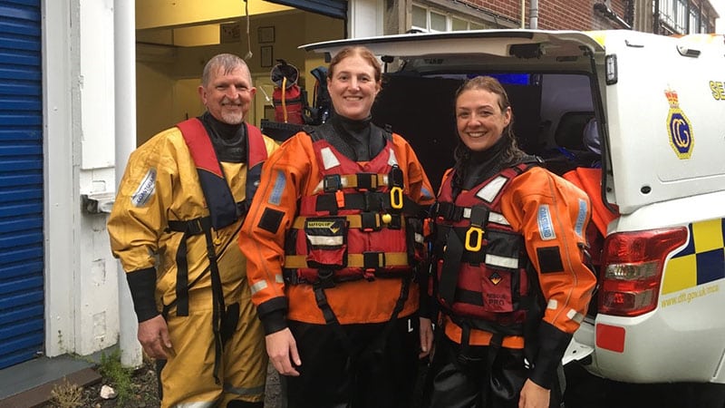 Three lifeboat volunteers in orange clothing smile at the camera