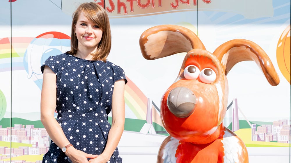 A young woman stands next to a statue of Gromit the dog