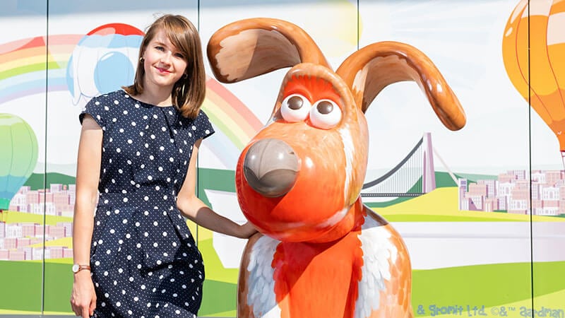 A young woman stands next to a statue of Gromit the dog