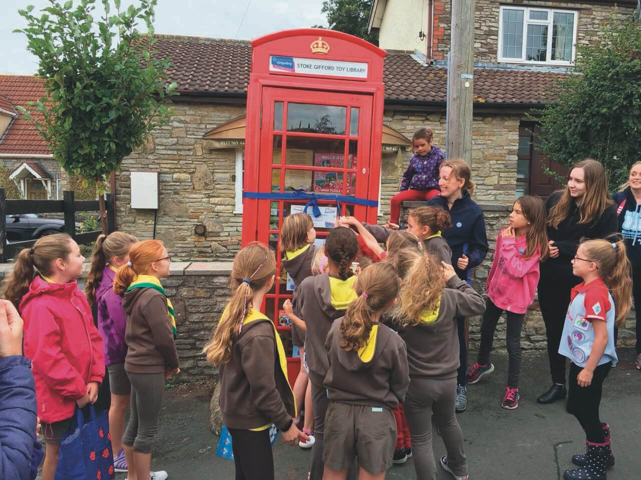 A group of children gathered around a red telephone box wrapped in a ribbon