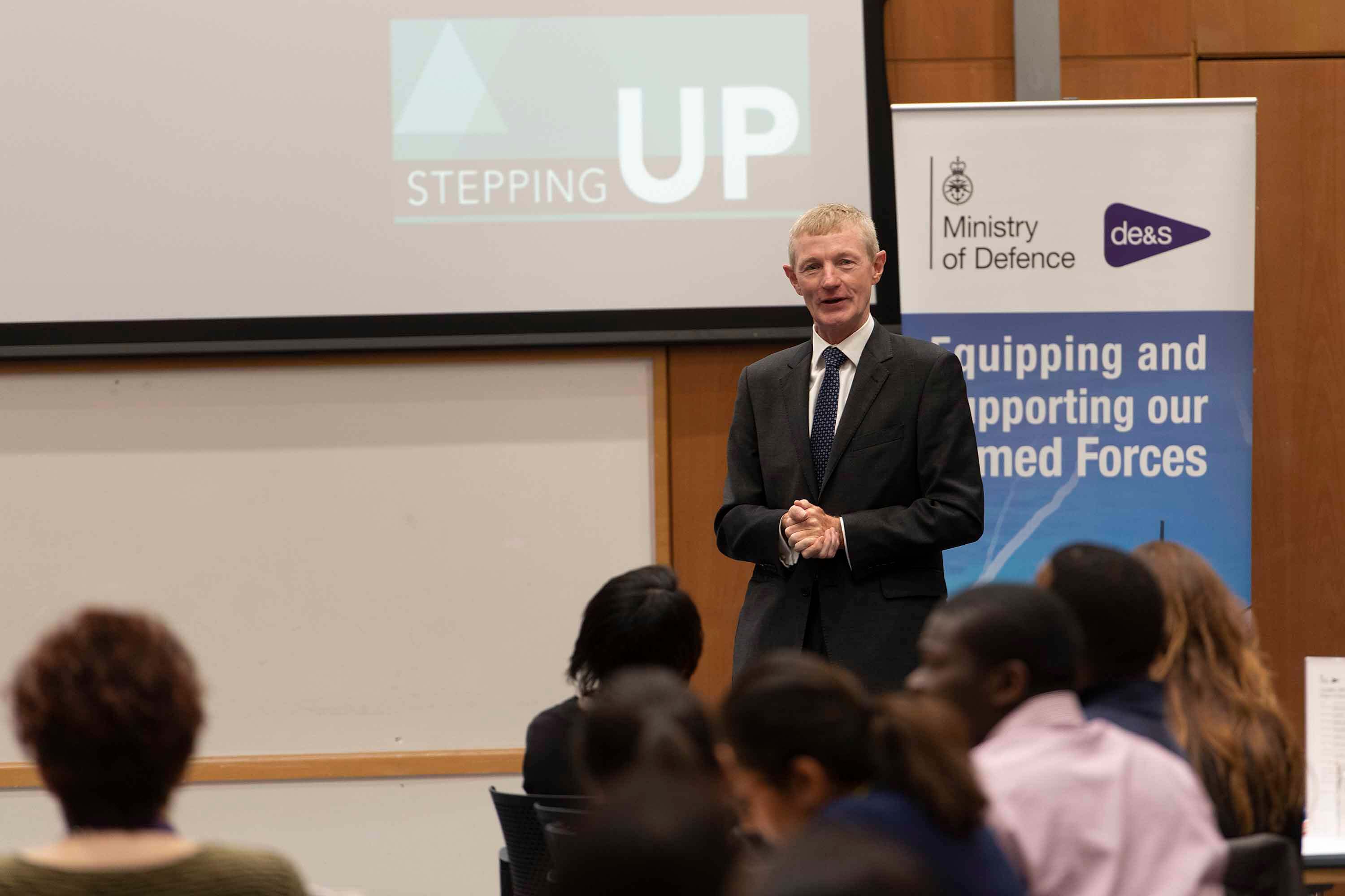 A man in a suit delivers a speech to a crowded room