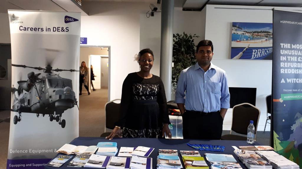 Two people stand in front of a display table covered in many different leaflets