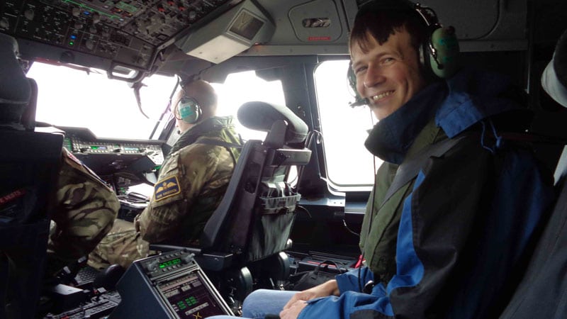 A young man smiles at the camera while wearing a headset, as he flies as a passenger inside a plane