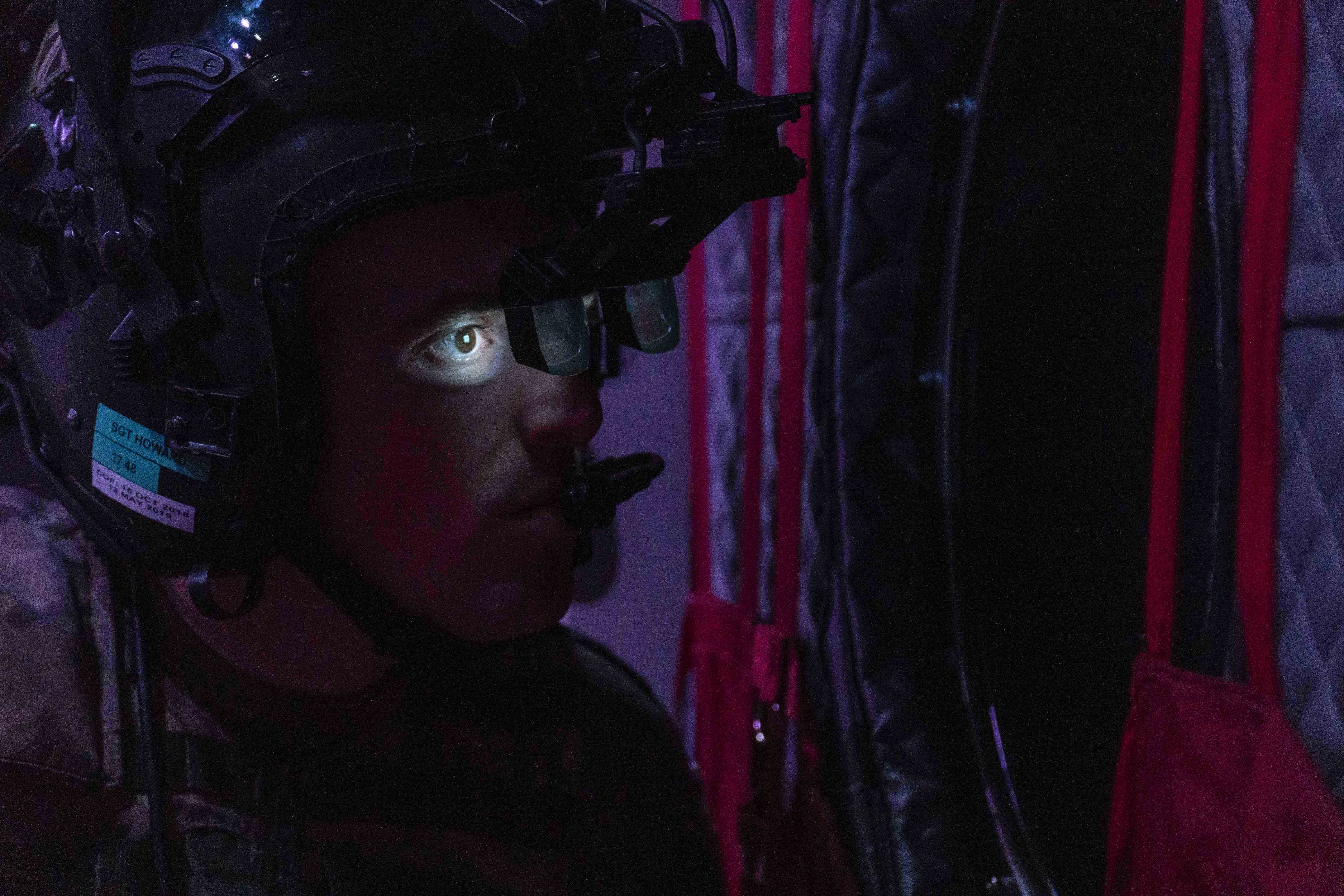 A solider's face is illuminated by the headset he wears inside a helicopter