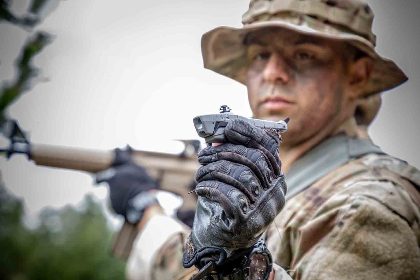 A soldier holds a small flying drone, smaller than the size of his hand