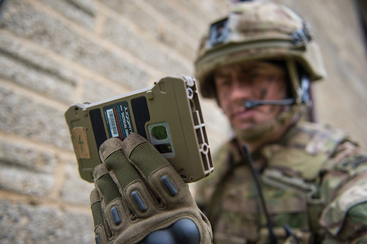 A soldier looking at a small handheld electronic device used to fly a drone