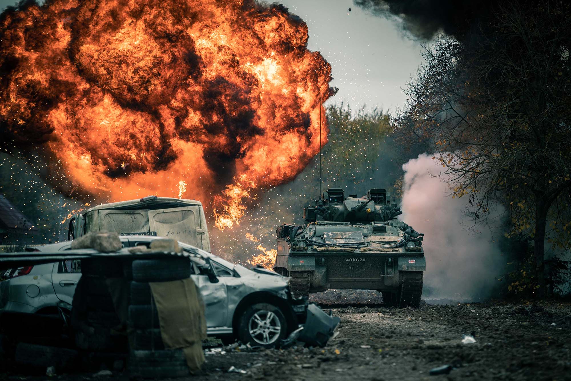 A tank driving away from a large fireball explosion during a training exercise