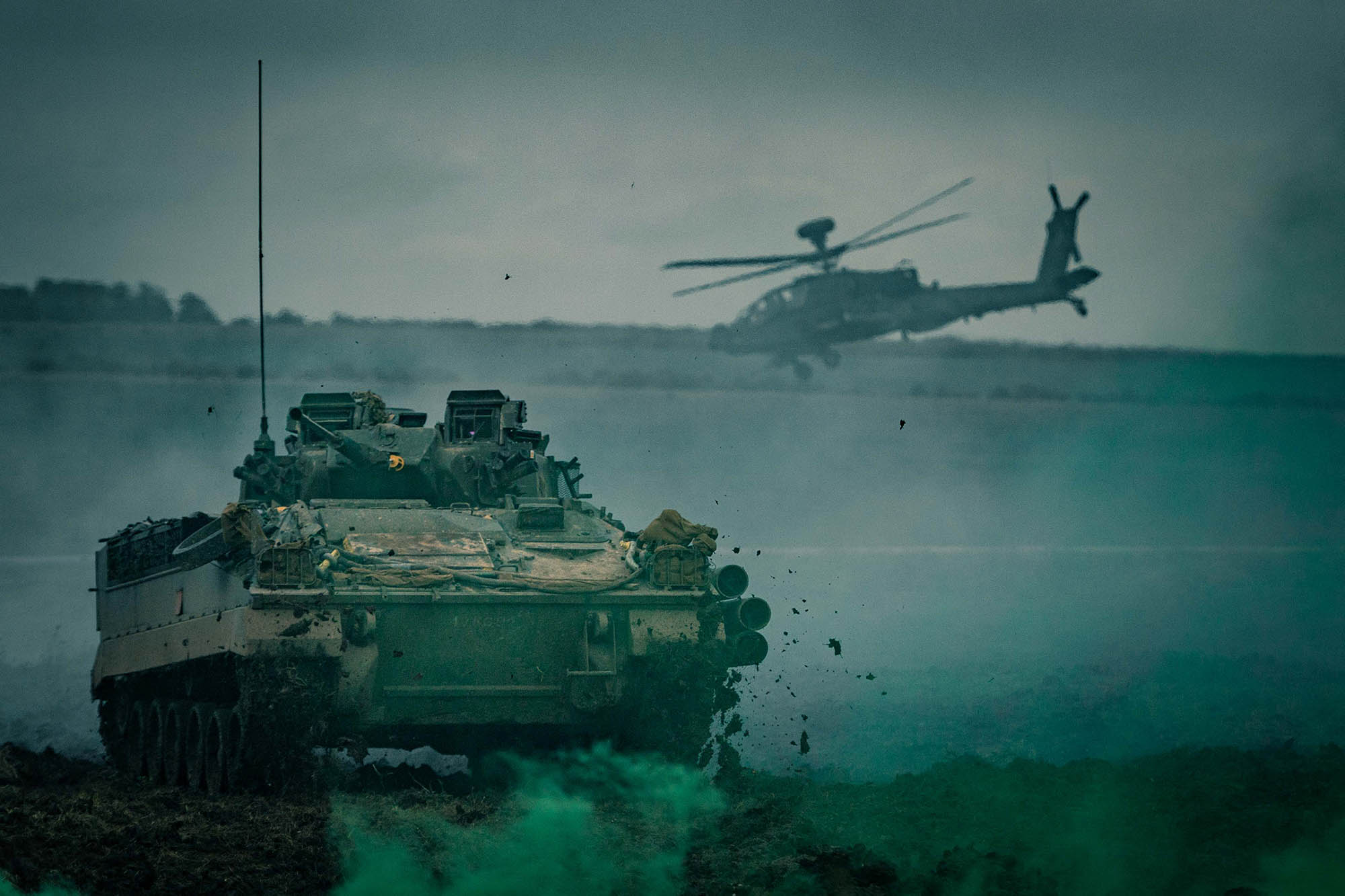 A tank driving in a muddy environment and a helicopter flying behind it
