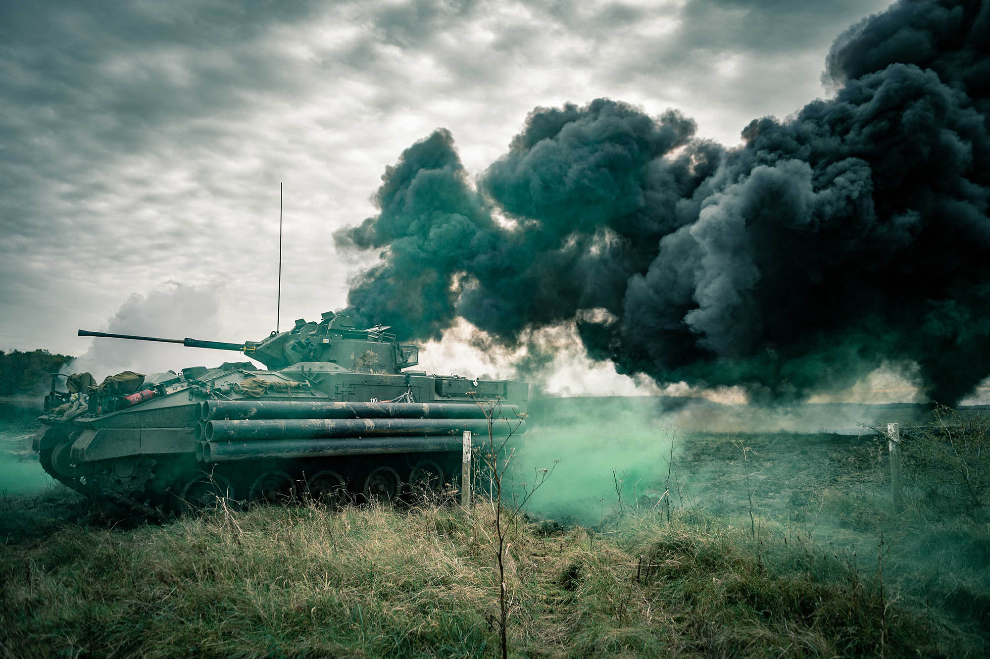 A tank in a field with black trail of smoke in the sky behind it