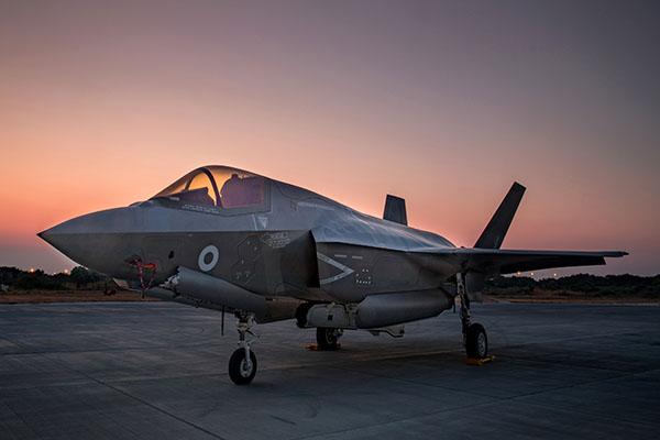 A large fighter plane stands on a runway at sunset
