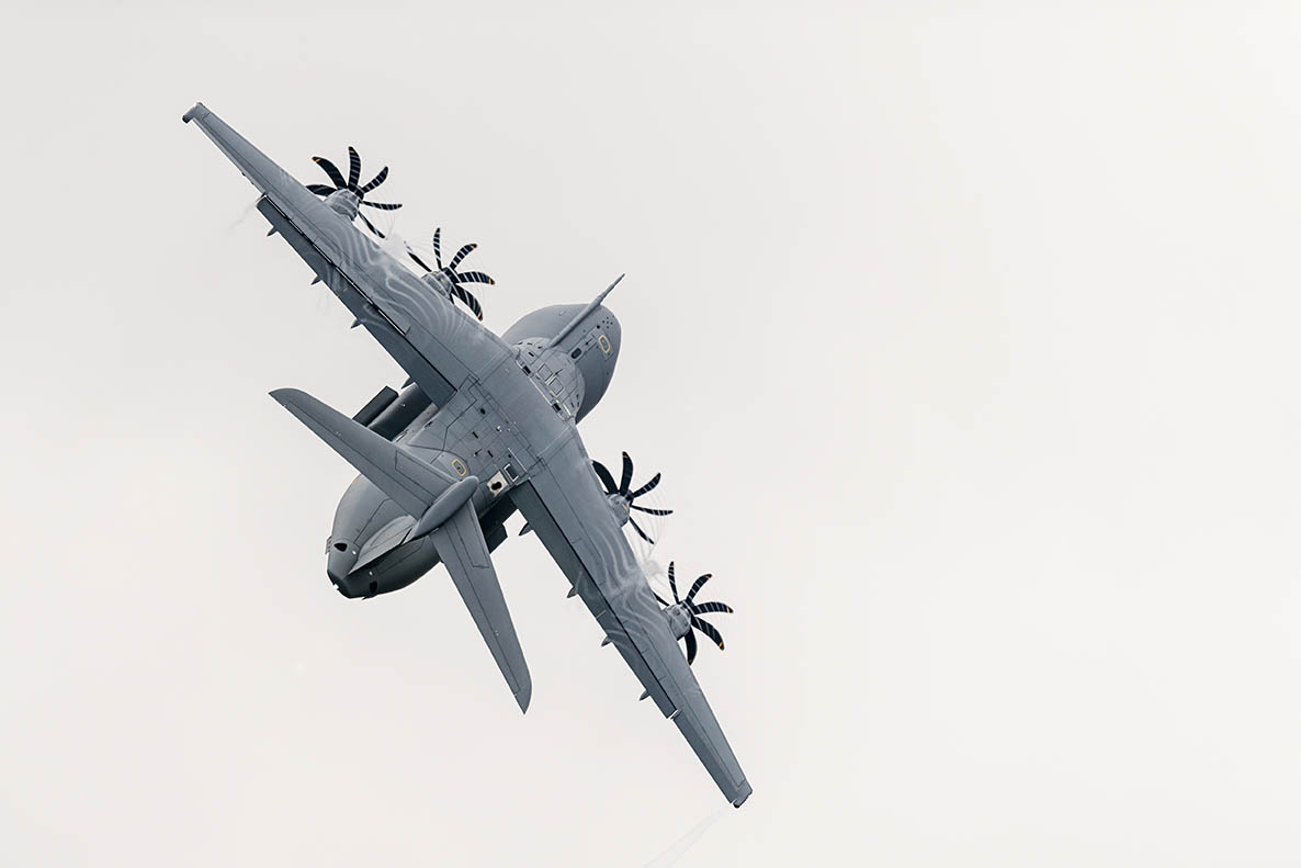 A large grey plane with propellers climbs steeply into the sky