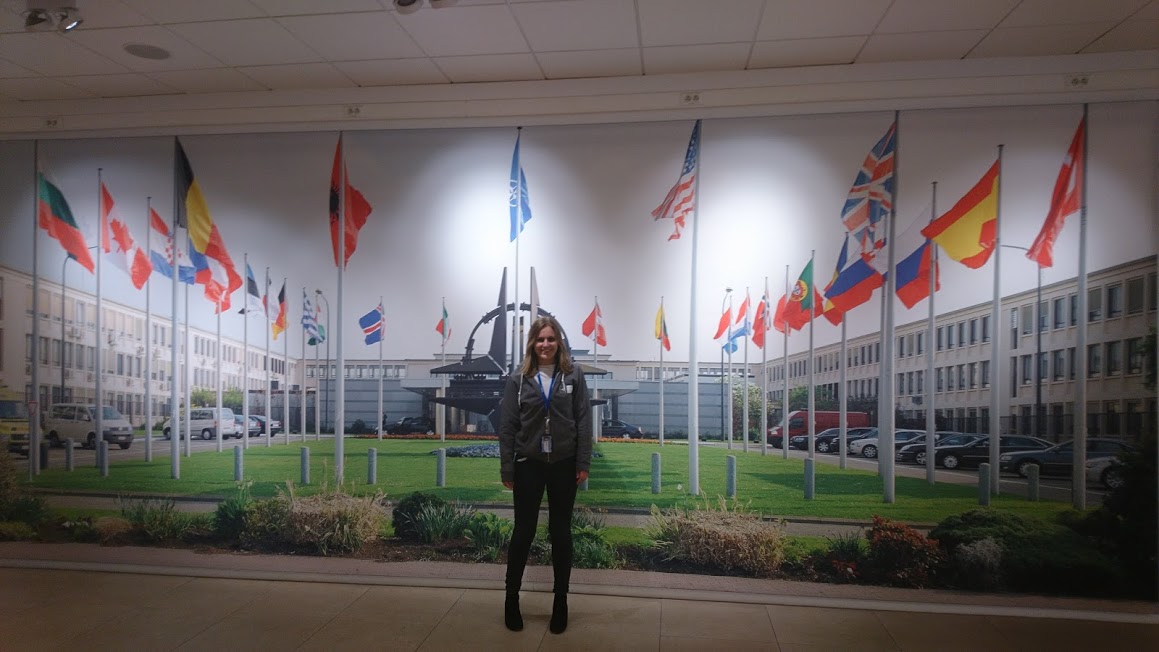 A lady stood against a wall with a picture of lots of different flags