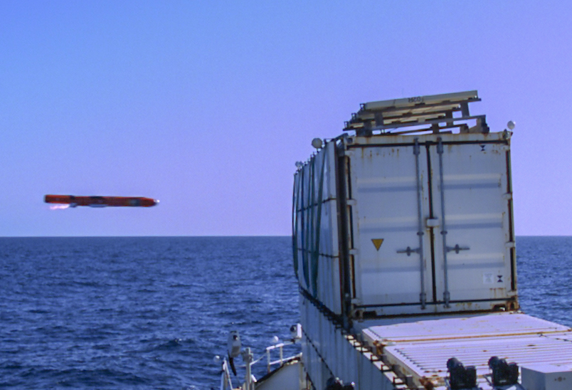 red missile flying towards a grey metal container at sea