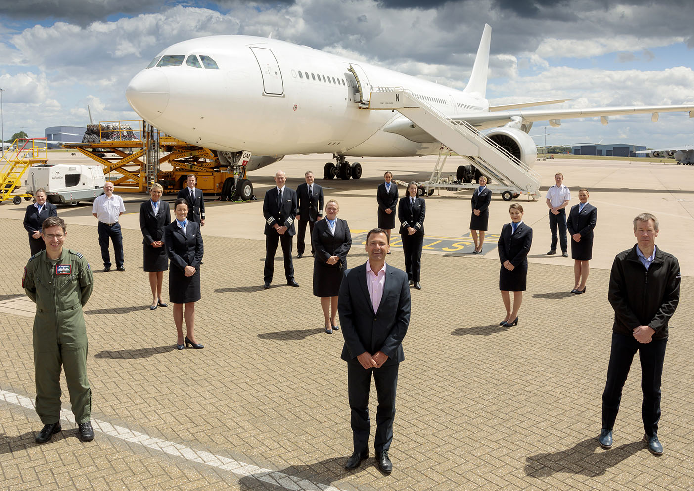 A number of air crew stood in suits and professional attire stood in front of a large airplane on a runway