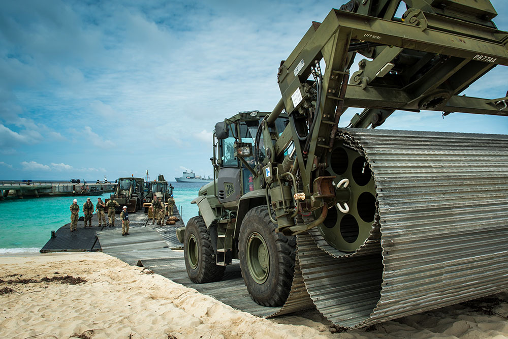 A bulldozer laying a temporary road on a tropical beach, having arrived on the sand via landing craft