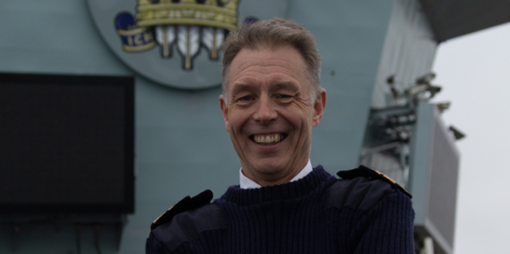 A head shot of a senior Navy Vice Admiral smiling in front of a ship