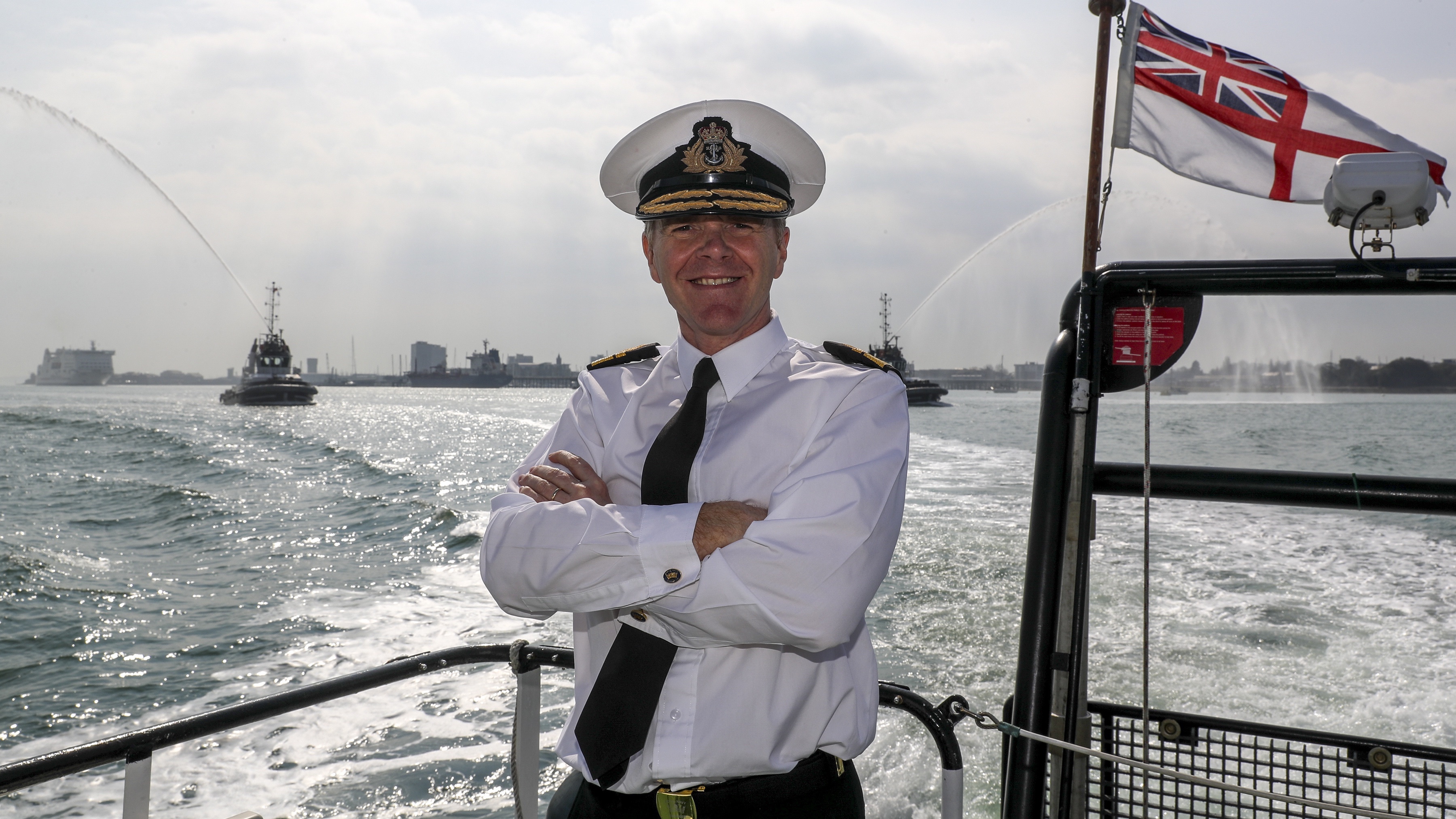 Navy officer stood facing the camera, on board a ship with the sea in the background