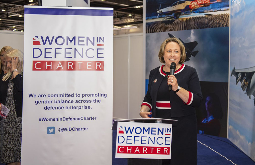 A female politician in a blue dress holds a microphone as she announces the launch of the Women in Defence Charter