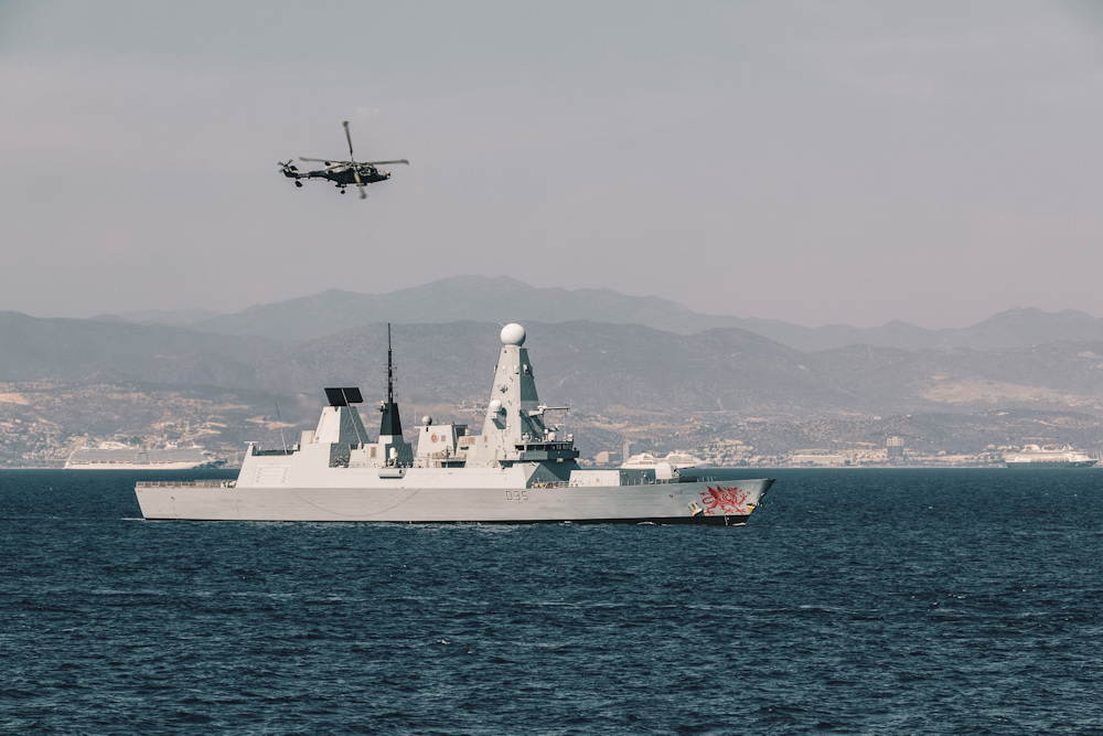 Type 45 destroyer HMS Dragon with a Wildcat helicopter flying overhead