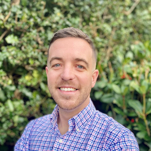 Air Safety and Environmental Manager Tom in a check shirt smiles in front of a green hedge